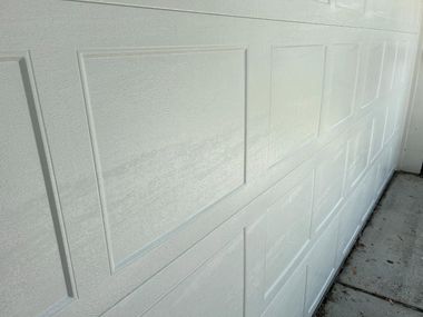 White garage door panels beside a concrete driveway with sunlight and shadows