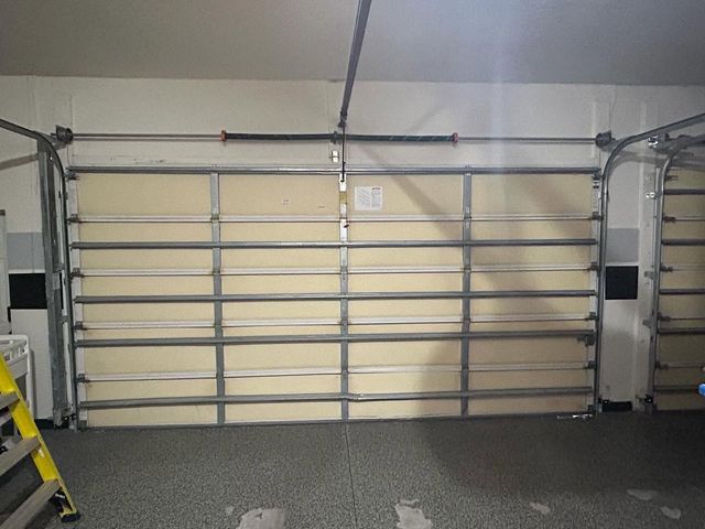 Closed garage door in a gray-walled garage, with a yellow step ladder on the left.
