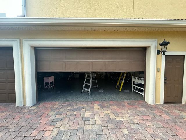 Open garage door with ladders and shelves inside, brick driveway outside.