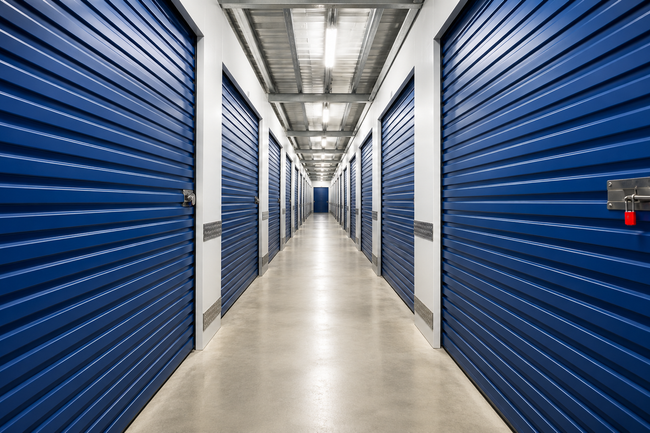 Blue storage unit hallway with rows of metal doors and a long beige floor corridor