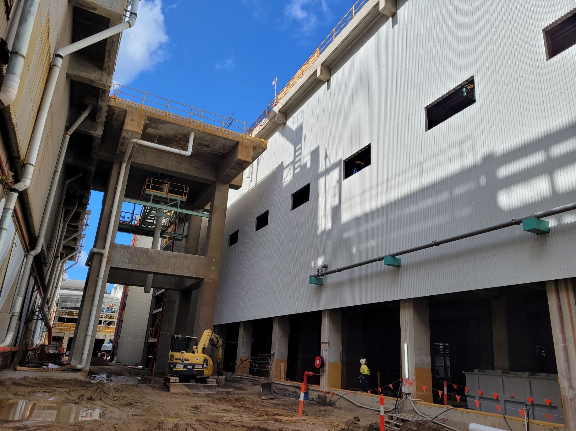Construction site with large gray building, excavator, exposed pipes, and workers under a blue sky — Construction Company in Townsville, QLD