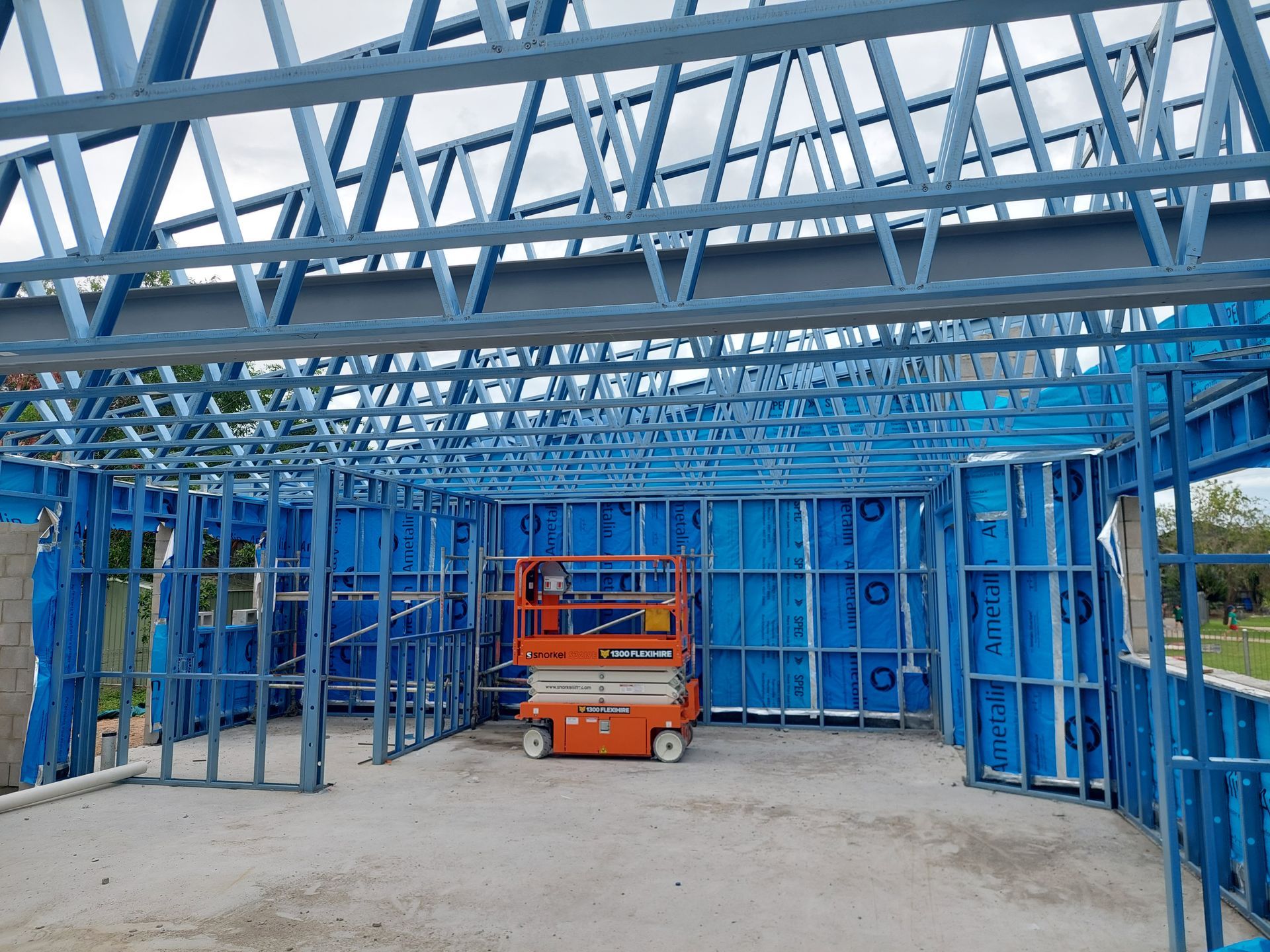 Blue steel frame construction of a building with an orange lift inside, under a cloudy sky — Construction Company in Townsville, QLD