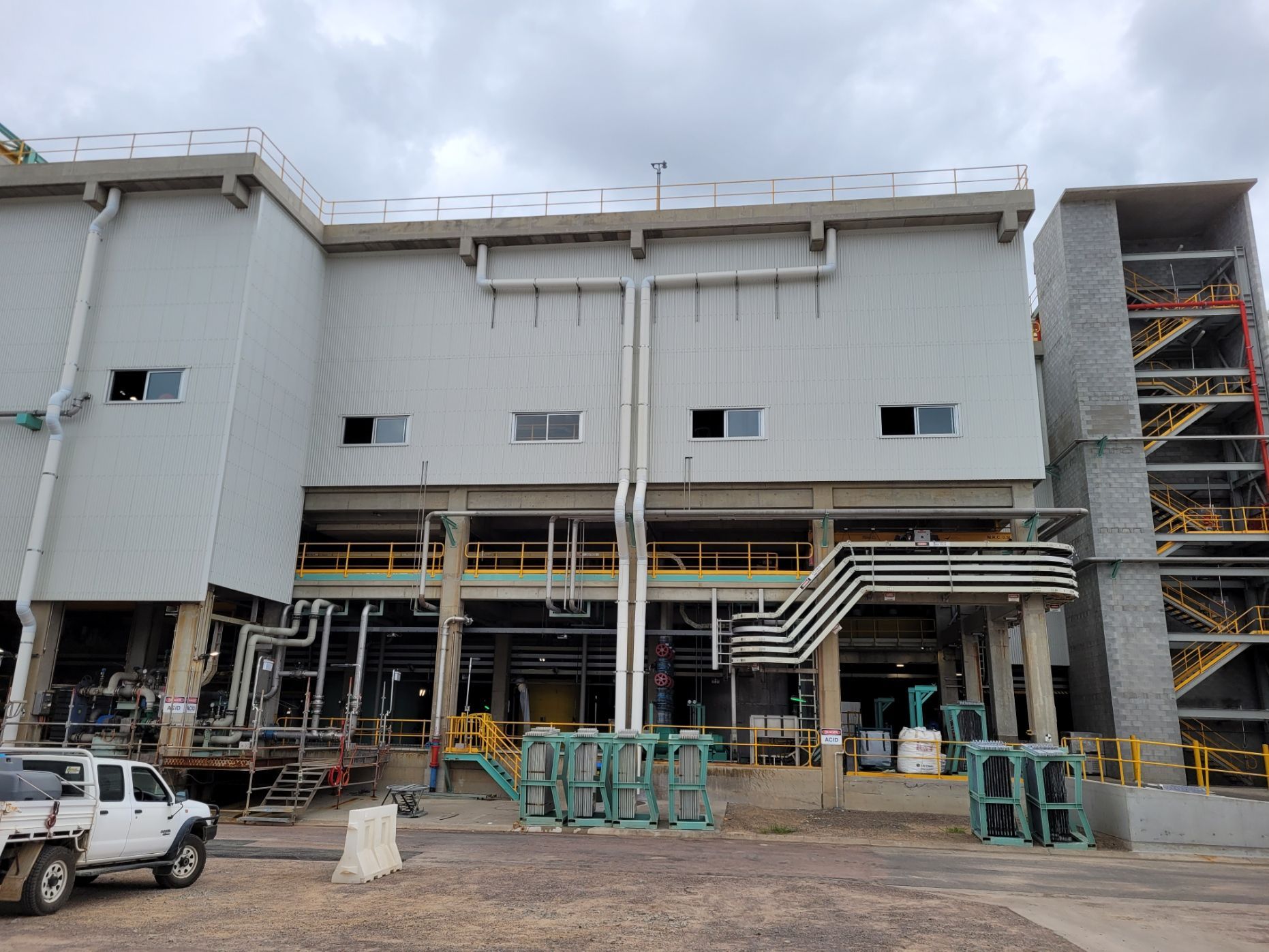 Exterior of a light gray industrial building with pipes, a truck, and a construction area under a cloudy sky — Construction Company in Townsville, QLD