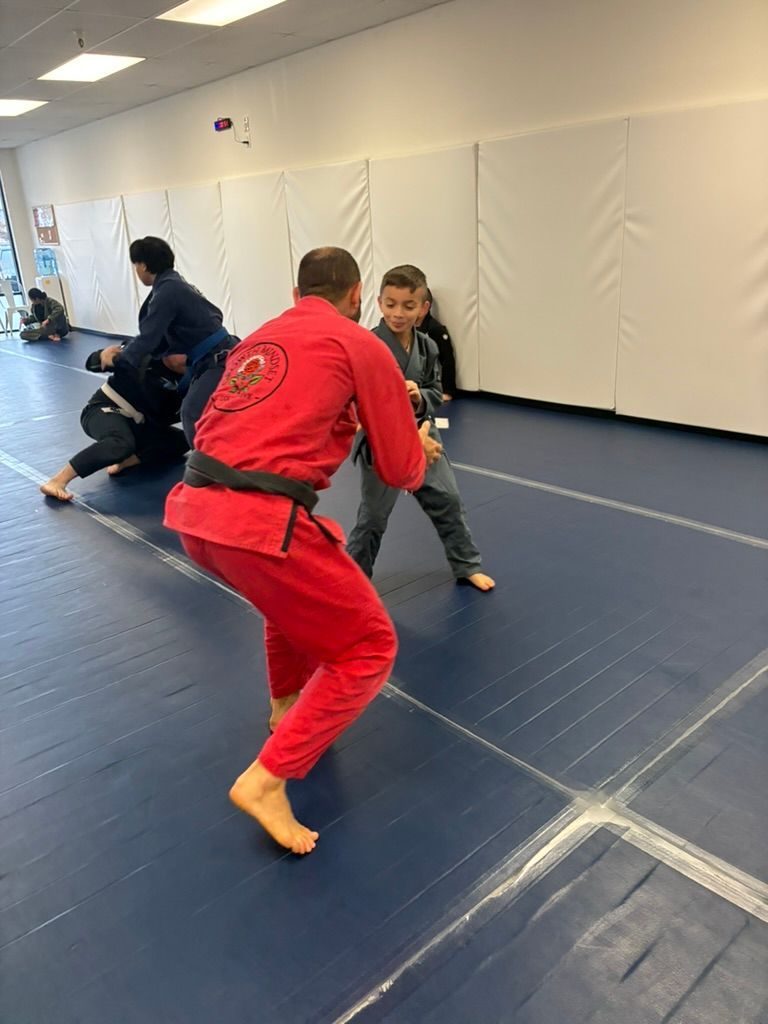 Martial arts practice on blue mats, instructor in red guiding a child in a gray gi