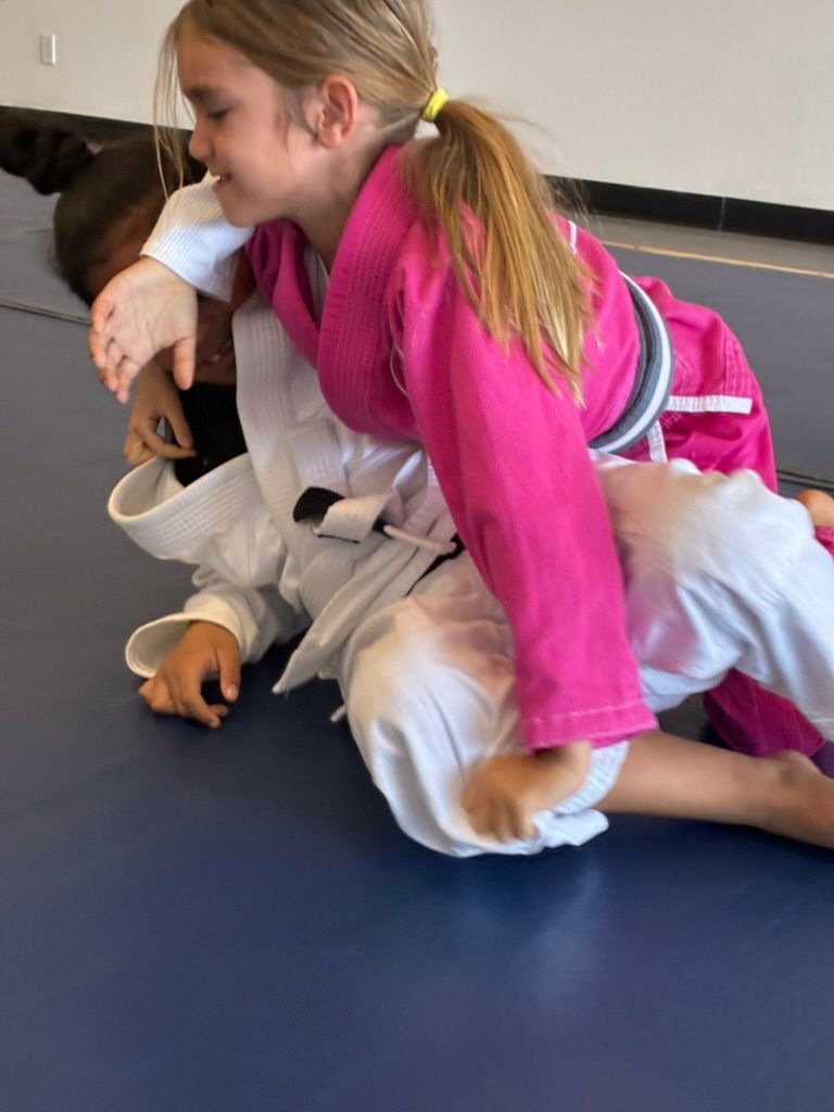 Two children in martial arts gis grappling on a blue mat during practice