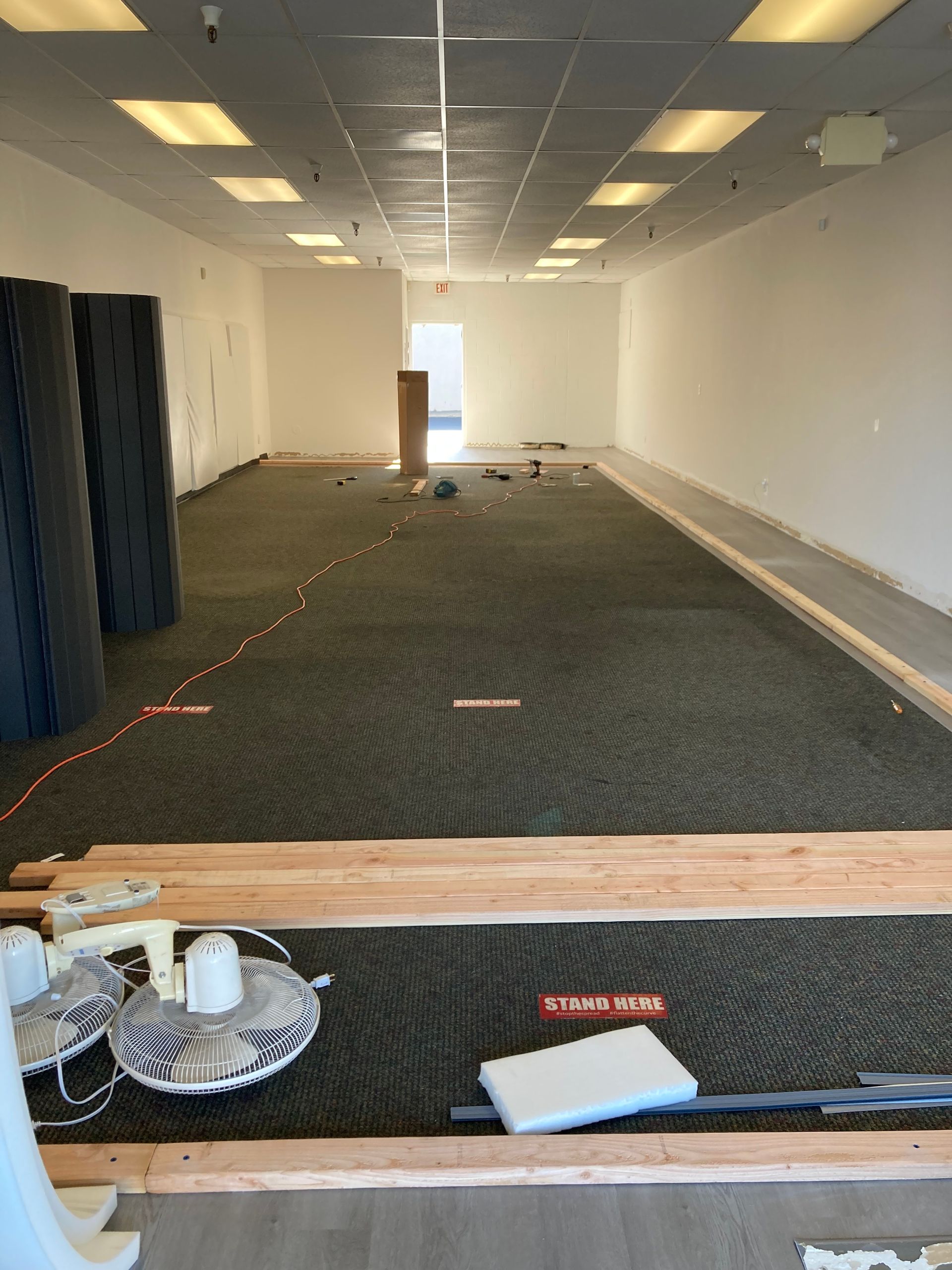 Empty office interior with carpet, white walls, ceiling lights, and a doorway at the far end