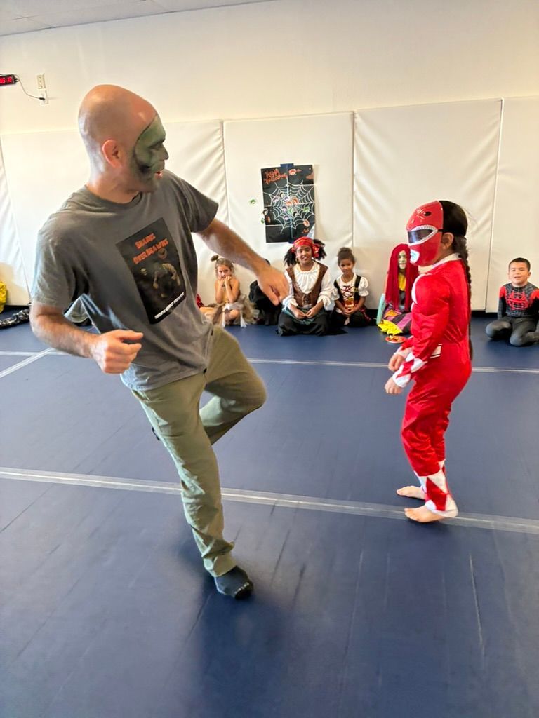 MMA instructor and child in red sparring on a blue mat in a training room