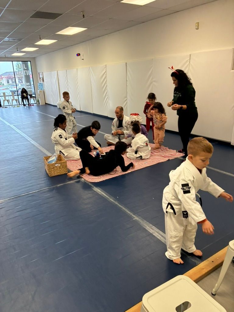 Children in white martial arts uniforms practice on mats in a bright studio with an instructor nearby