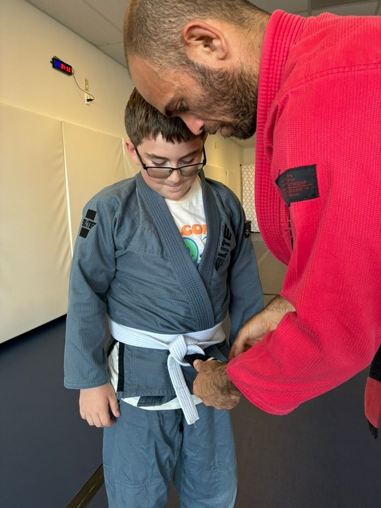 Adult helping child tie a martial arts belt indoors