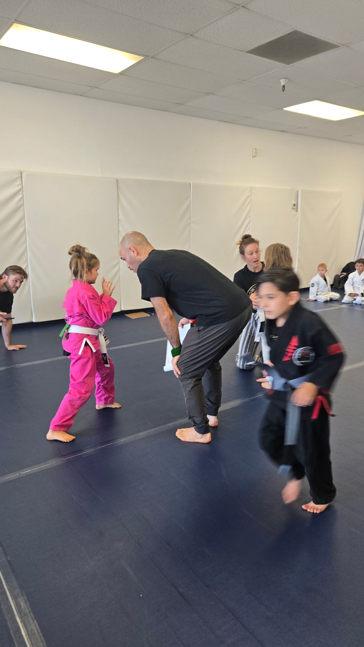 Children practicing martial arts on blue mats with an instructor in a bright studio