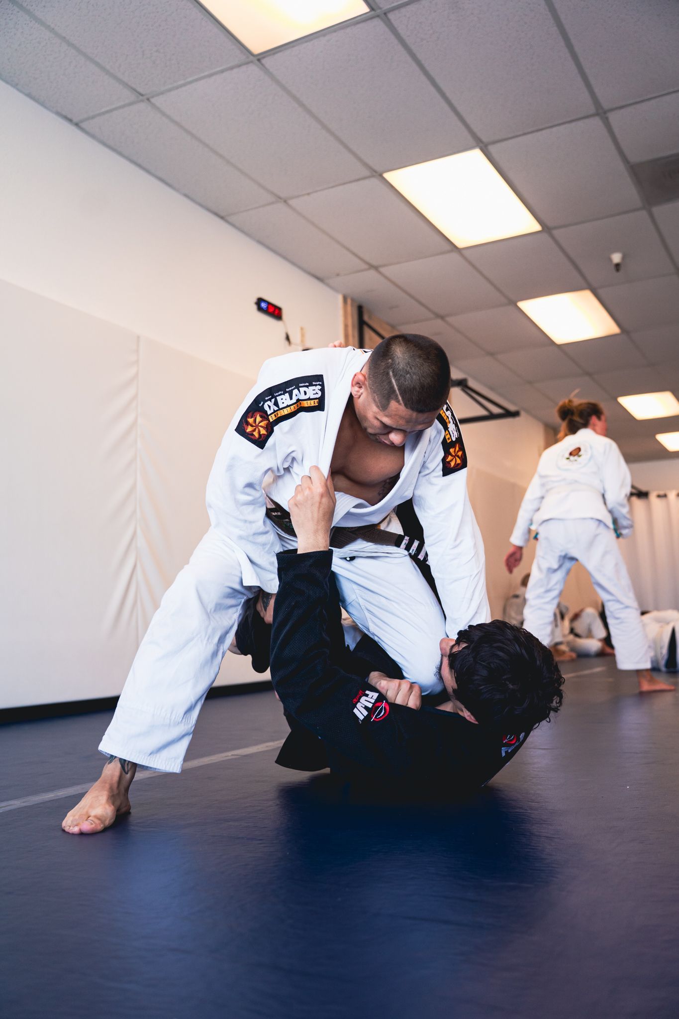 Two martial artists practicing grappling on a mat in a bright training studio