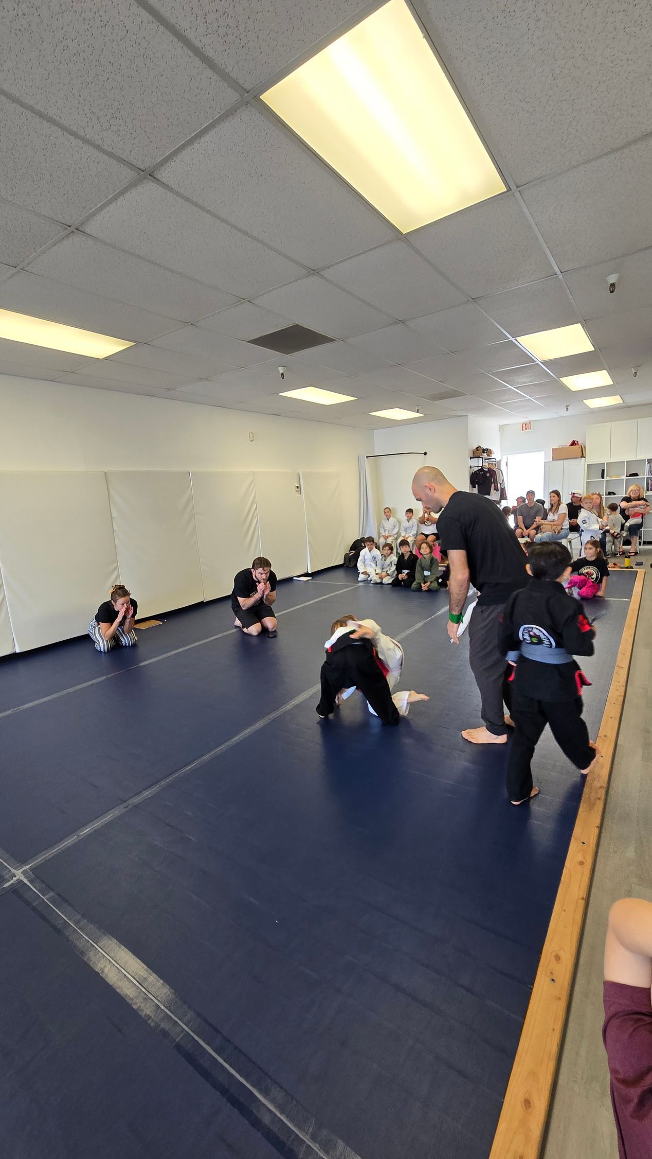 Kids practicing gymnastics on blue mats in a bright indoor studio, with an instructor nearby.