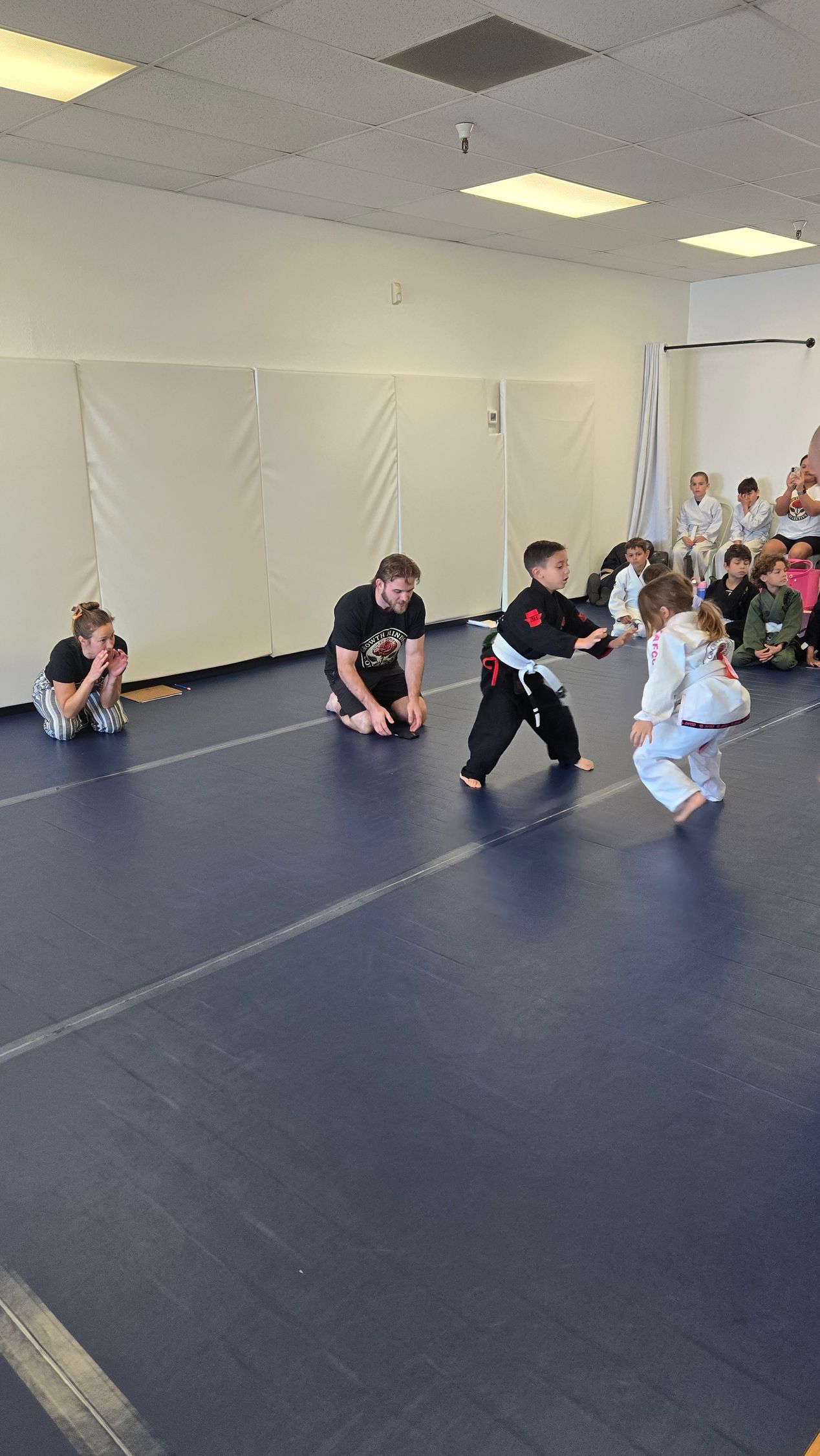 Children in martial arts uniforms practicing on blue mats in a gymnasium class