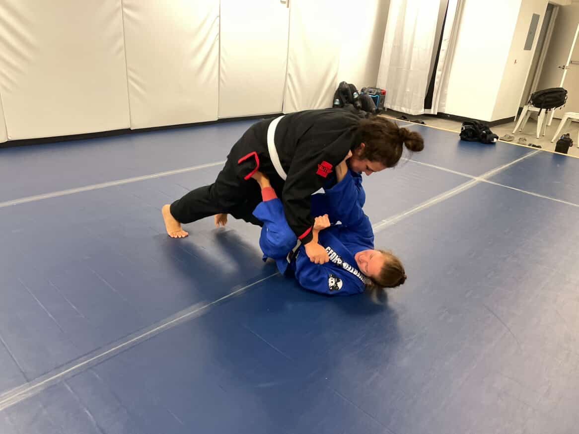 Two people practicing grappling on blue mats in a martial arts gym