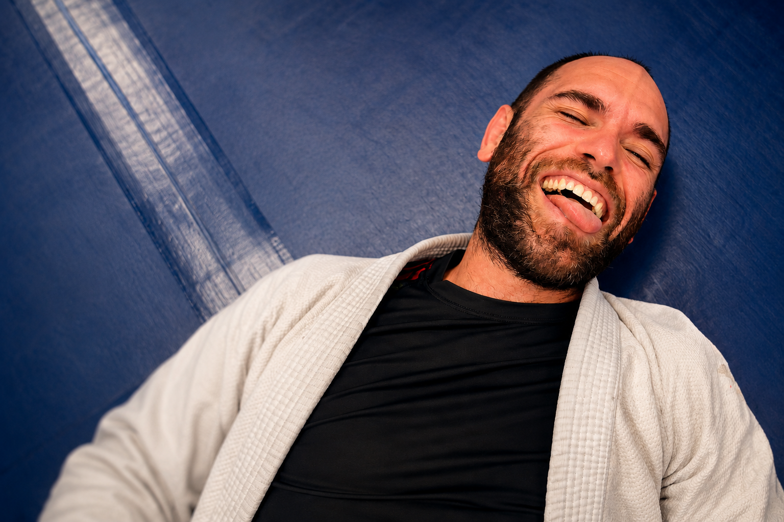 Smiling man in a white sweater and black shirt, leaning against a blue backdrop