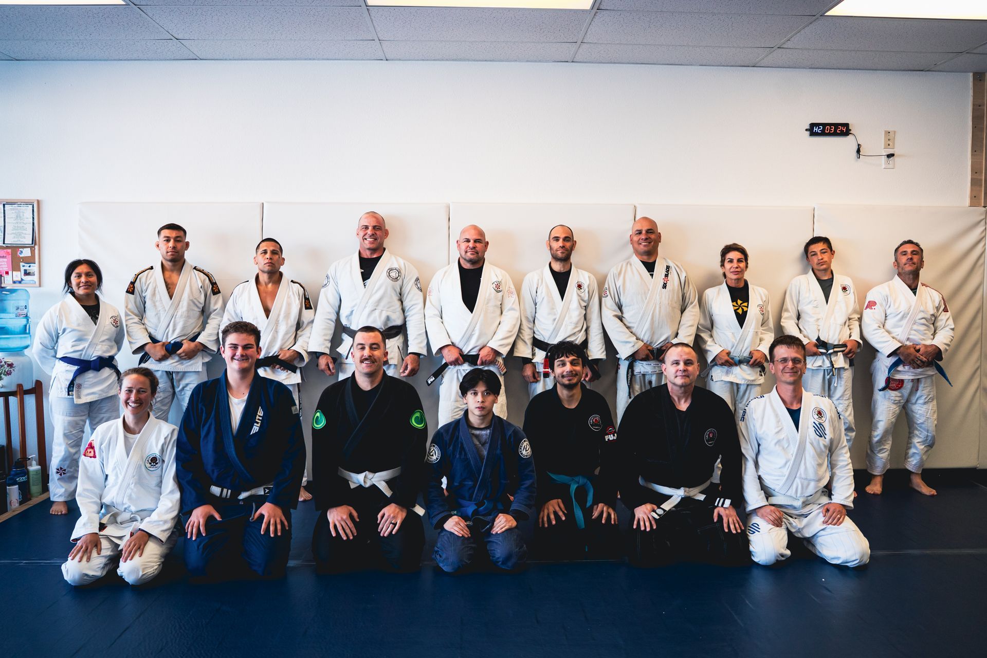 Group photo of jiu-jitsu students and instructors in white and black gis in a dojo