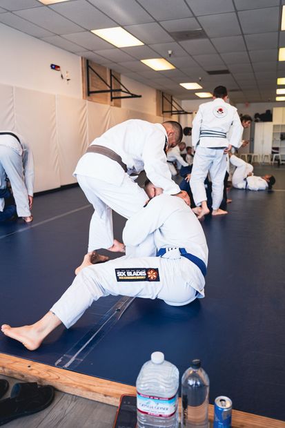 Brazilian jiu-jitsu class on mats, with students in white gis practicing grappling indoors.