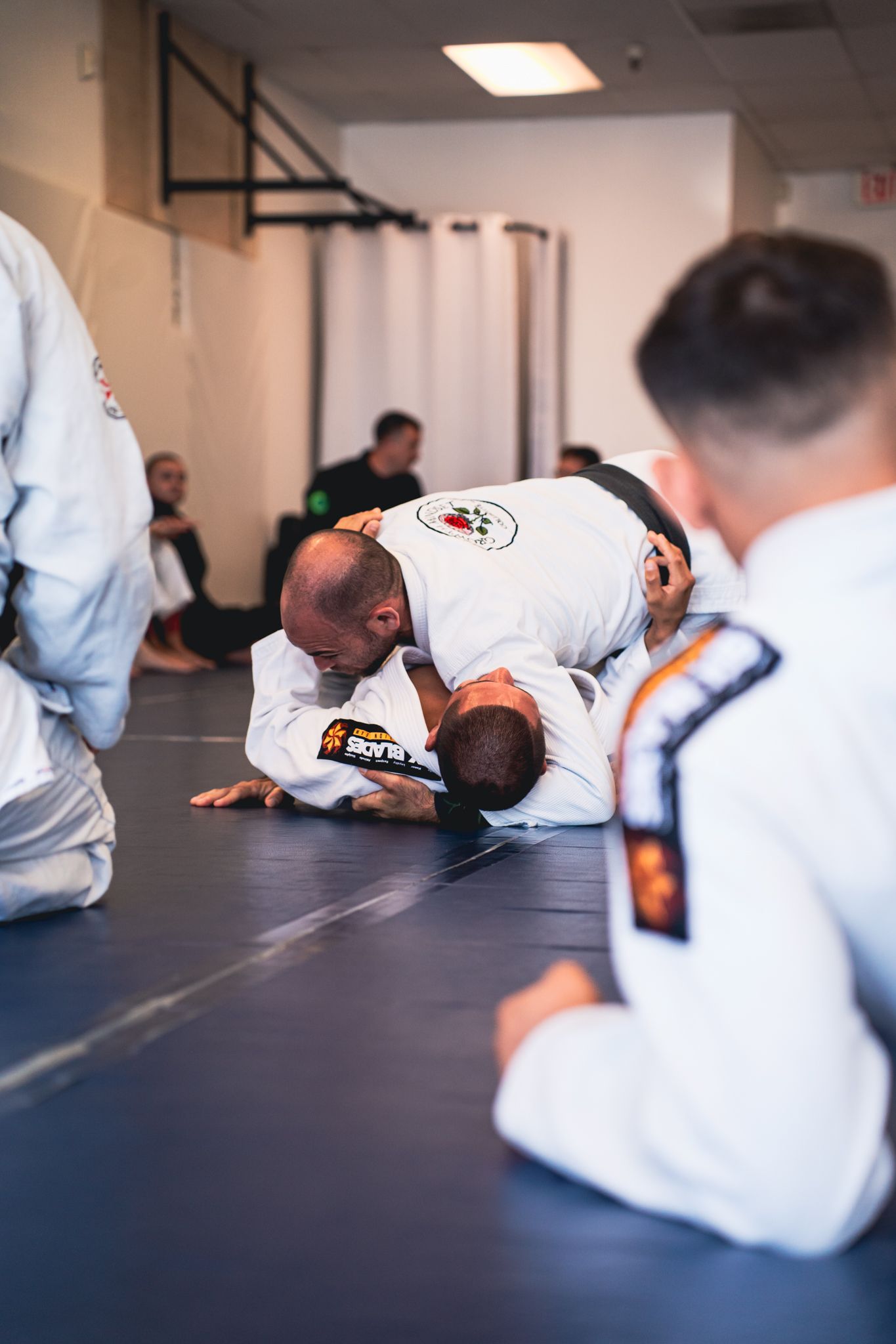 People in white gis practicing grappling on a mat in a martial arts studio