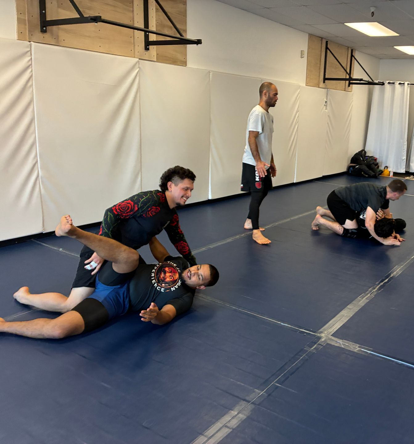 Mats in a martial arts gym with people grappling and practicing jiu-jitsu drills.