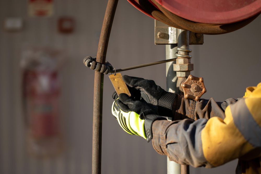 A Man Wearing Gloves Is Working on A Pipe — Fireline 2000 Fire Equipment Pty Ltd in Browns Plain, QLD