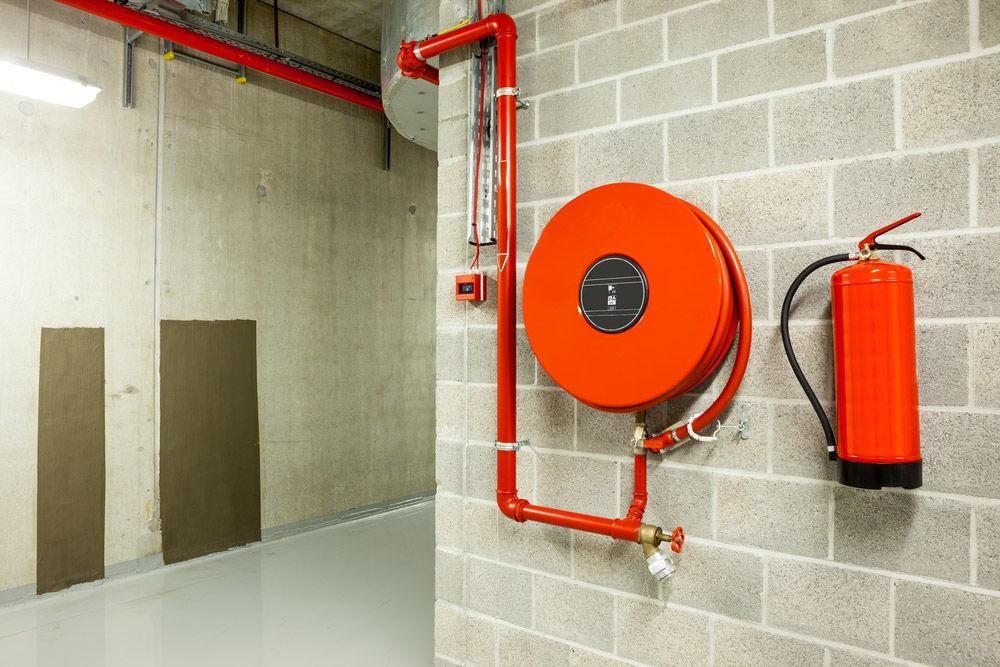 A Red Fire Hose Reel Is Attached to A Brick Wall Next to A Fire Extinguisher — Fireline 2000 Fire Equipment Pty Ltd in Brisbane, QLD