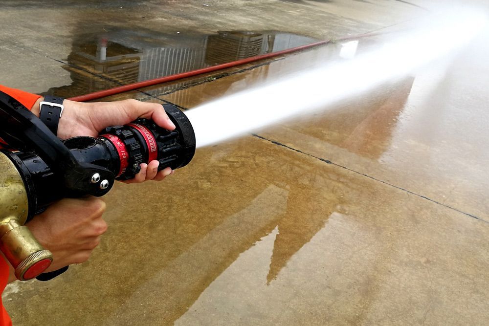 A Person Is Holding a Fire Hose and Spraying Water on The Ground — Fireline 2000 Fire Equipment Pty Ltd in Browns Plain, QLD