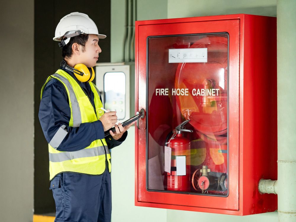 A Man Is Standing in Front of A Fire Hose Cabinet — Fireline 2000 Fire Equipment Pty Ltd in Browns Plain, QLD