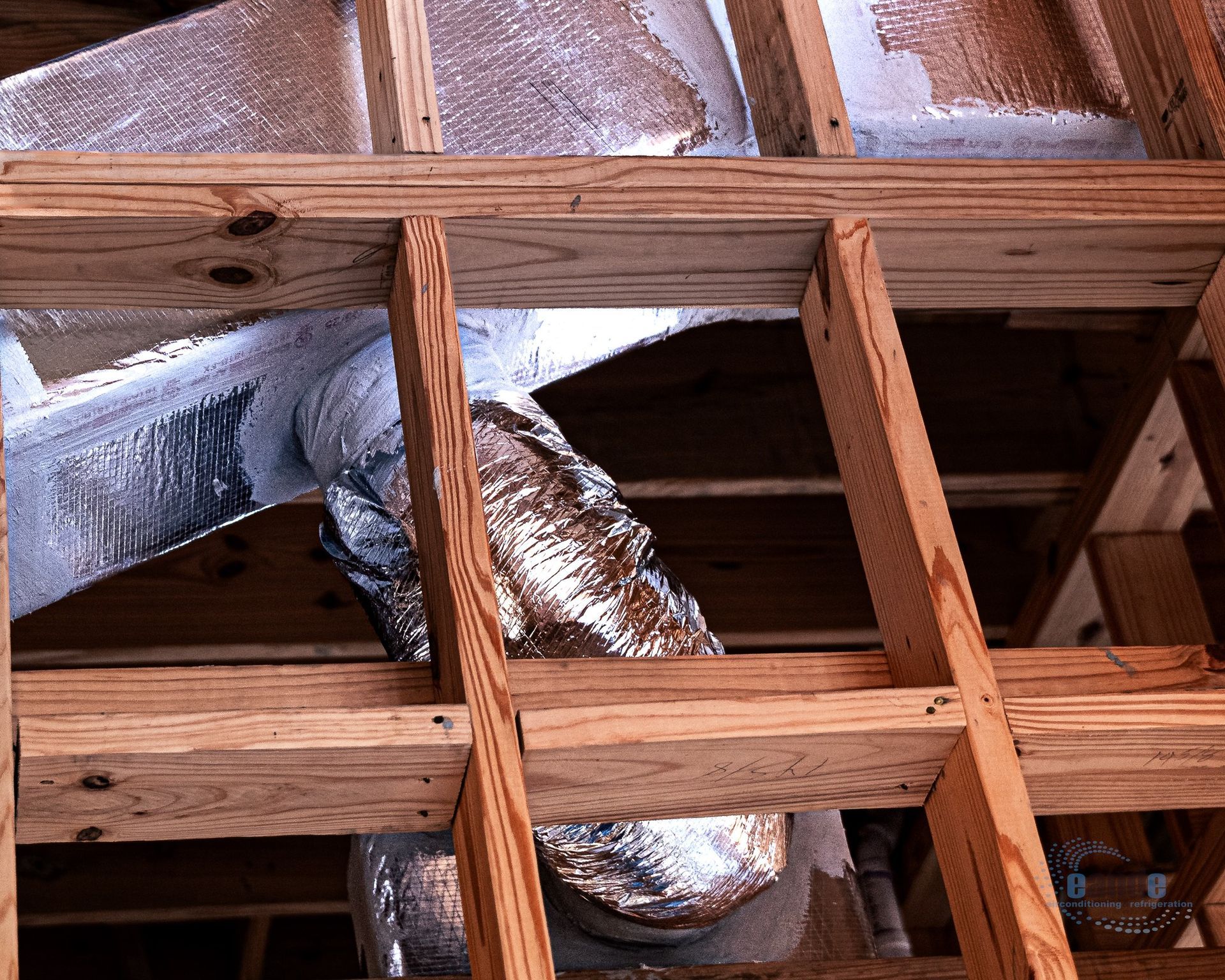 Exposed attic framing with silver insulated ductwork running through wooden joists and rafters