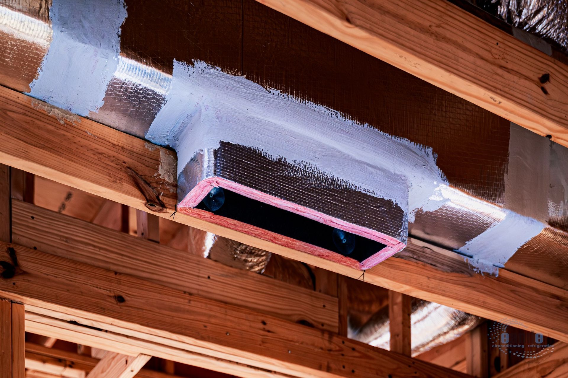 Open ceiling vent duct wrapped in white insulation between exposed wooden beams