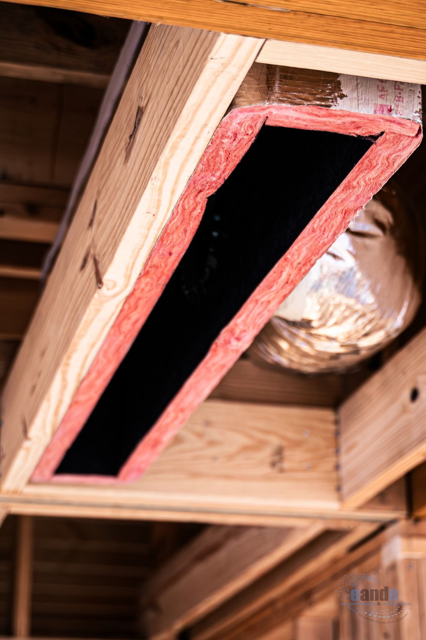 Wooden attic hatch with pink insulation lining and a dark opening in the ceiling