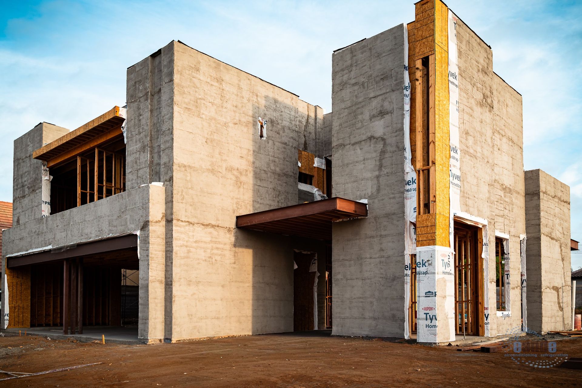 Unfinished concrete modern house under construction with wood-framed windows and brown dirt foreground