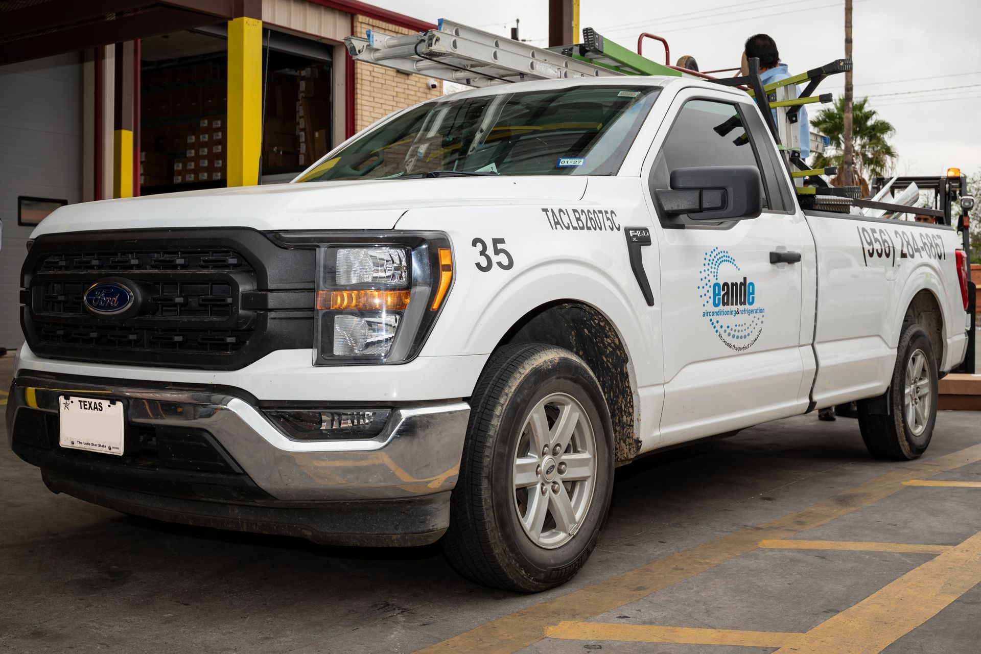 White utility pickup truck parked beside a building, with workers in the bed and vehicle number 35 on the side.