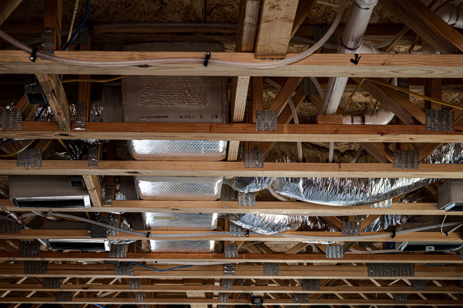 Exposed wooden ceiling joists with ducts and insulation in an unfinished interior construction site