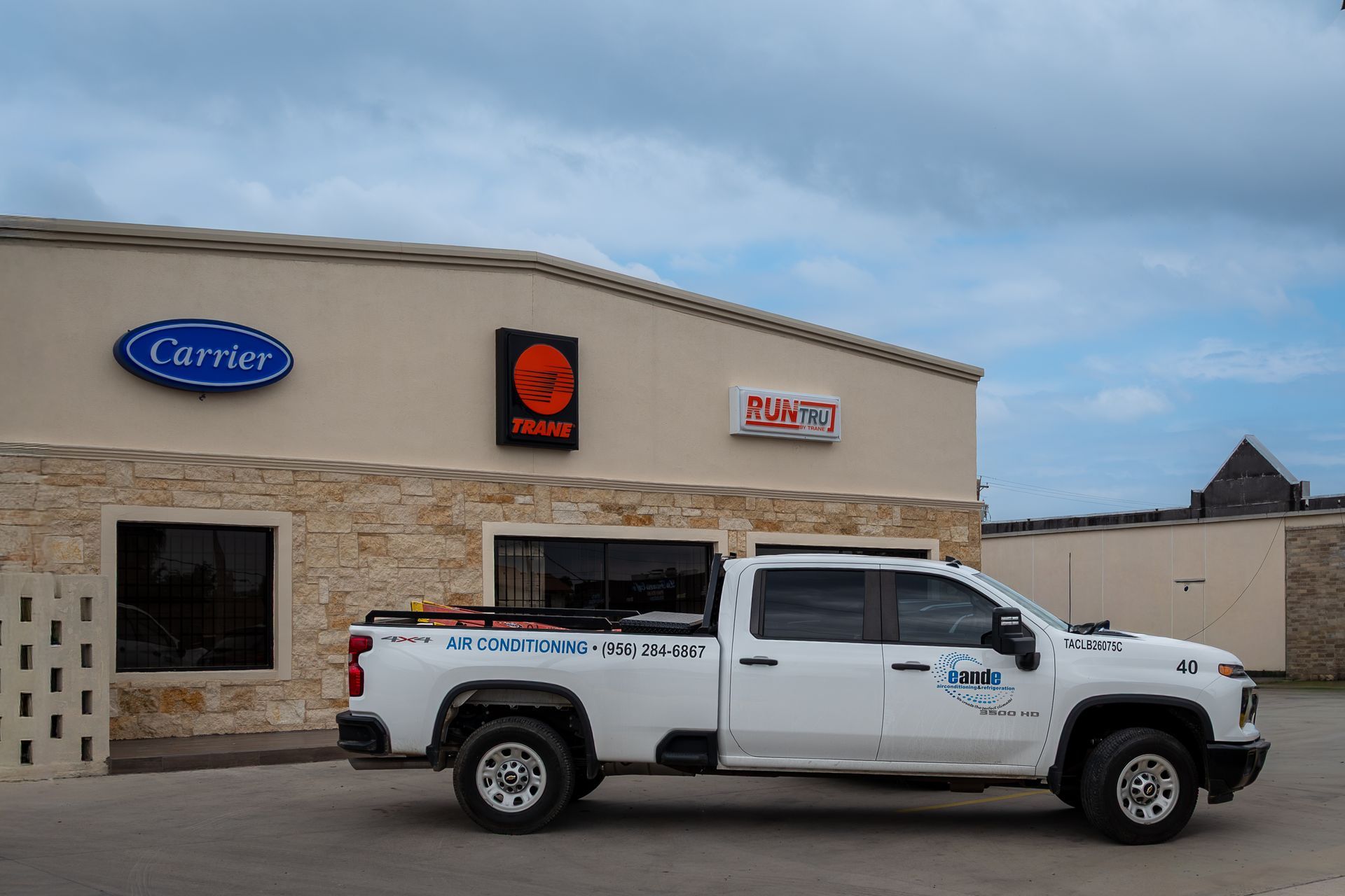 White pickup truck parked outside a tan commercial building with business signs under a cloudy sky