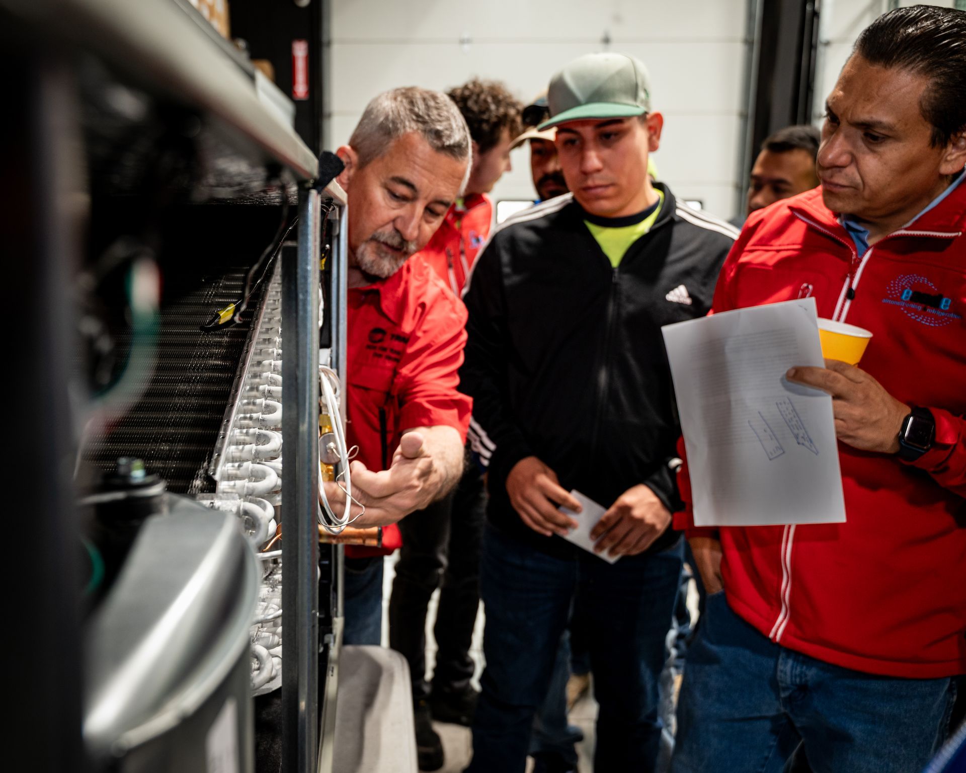 Three people inspect machinery in a workshop, one holding papers, with focused expressions.