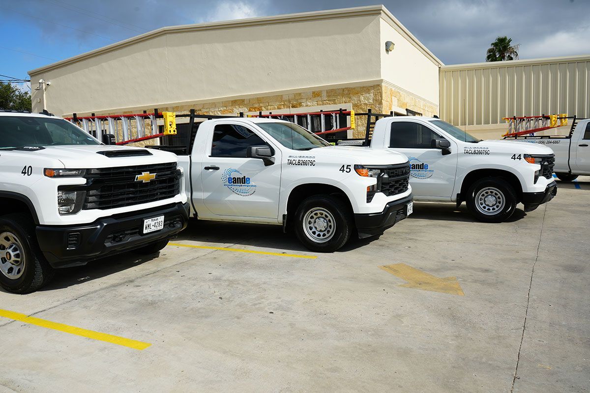 Three white pickup trucks parked in a lot beside a beige building