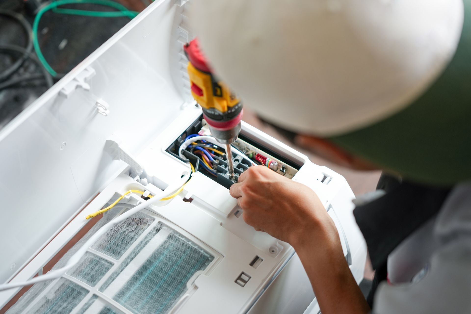 Technician wiring a white industrial panel with a yellow tool in a factory setting