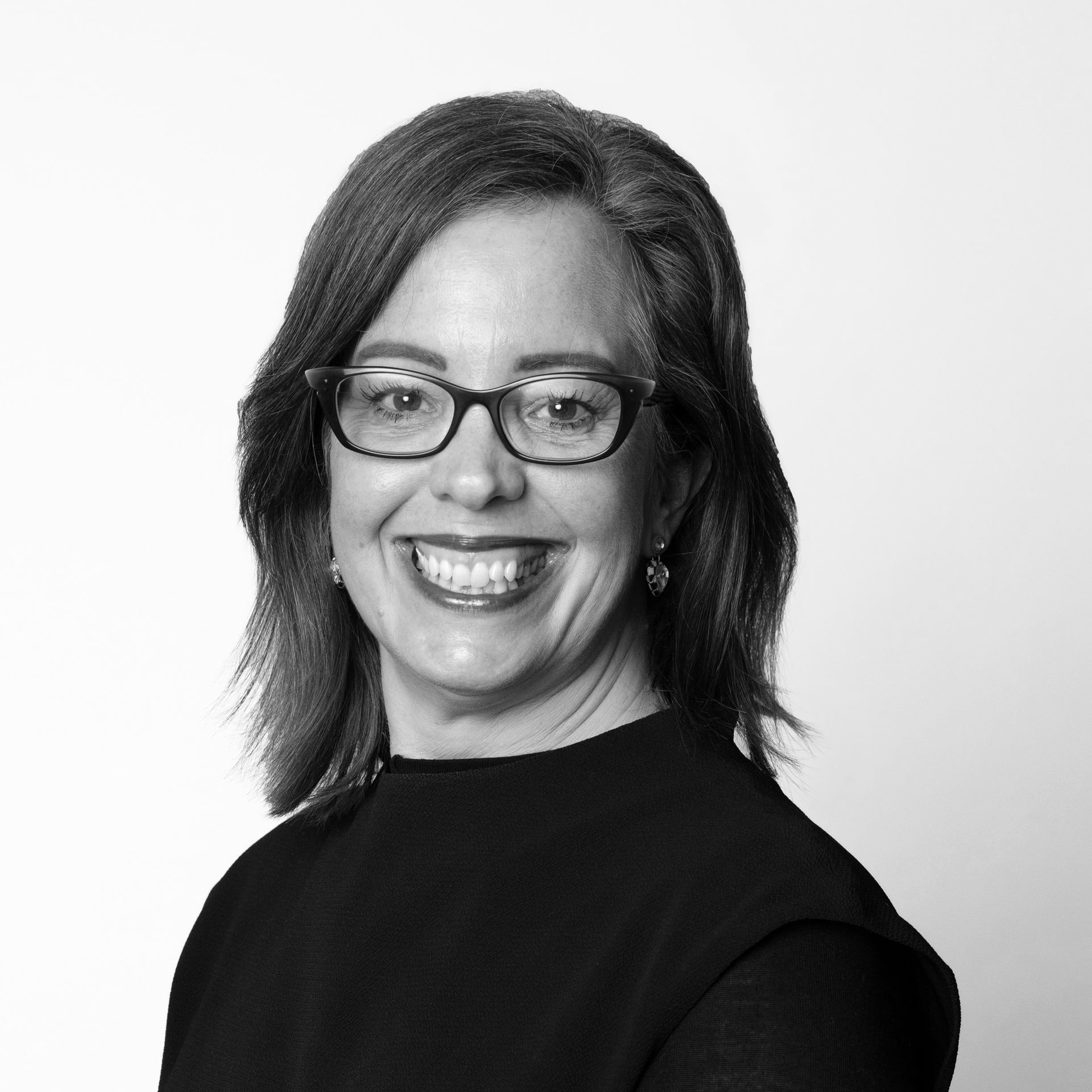 Portrait of a smiling woman with glasses in a dark top against a light background