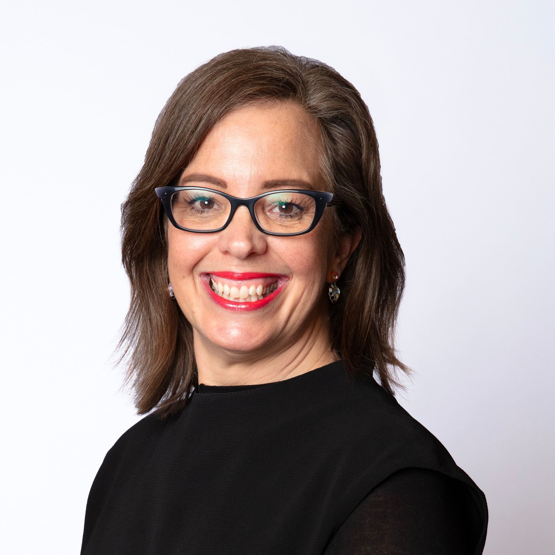 Smiling person with glasses and shoulder-length hair, wearing a black top on a light background