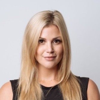 Blonde woman with straight hair in a black sleeveless top, facing forward against a light gray background