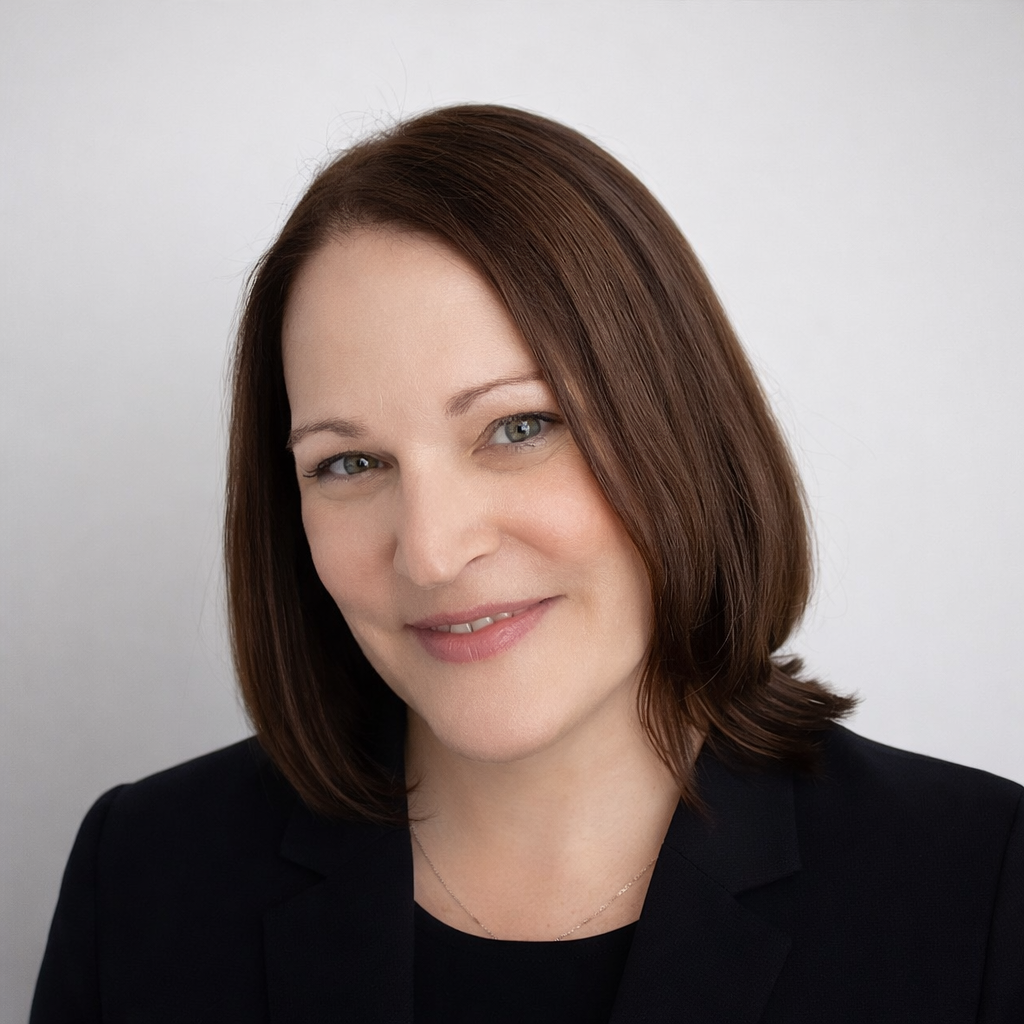 Portrait of a smiling woman with shoulder-length brown hair in a dark blazer on a light background