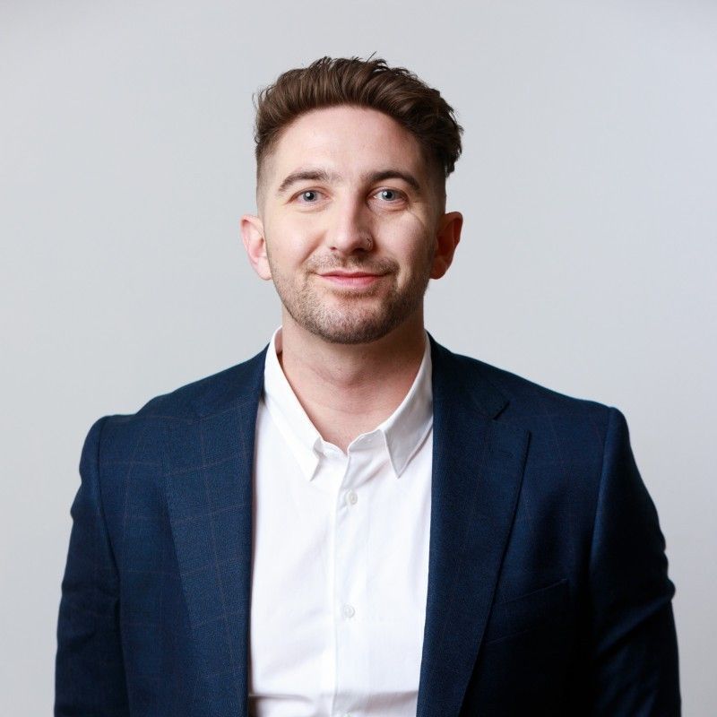 Smiling man in a navy blazer and white shirt against a light gray background