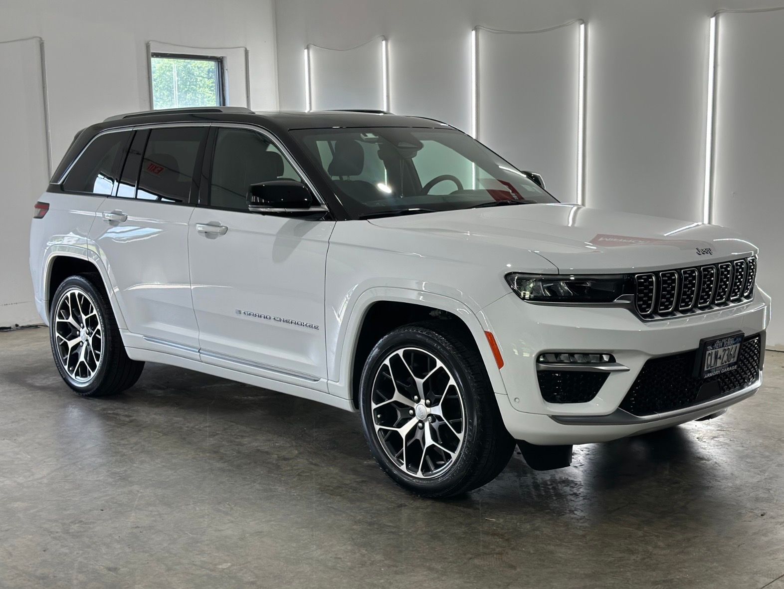 A white Jeep Grand Cherokee SUV with a black roof and custom multi-spoke wheels, parked in a bright, modern garage.