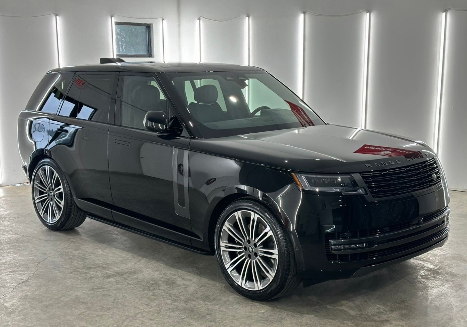 A black Range Rover parked in a brightly lit, sterile studio with vertical white light panels on the walls.