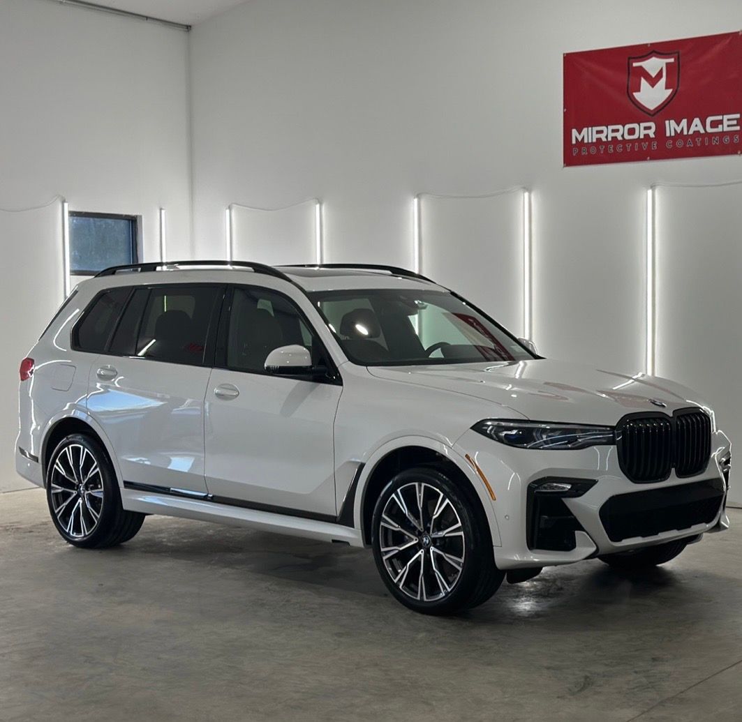 A white BMW X7 SUV with black rims and grille parked inside a well-lit showroom with a 