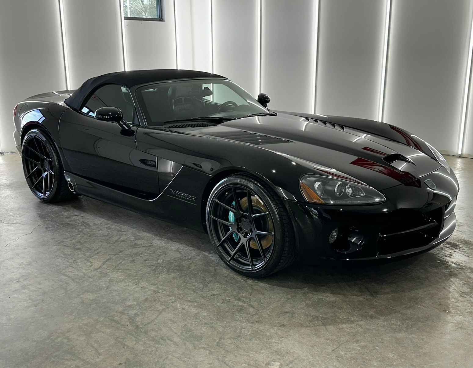 A sleek, glossy black convertible Dodge Viper parked in a brightly lit studio with white walls.