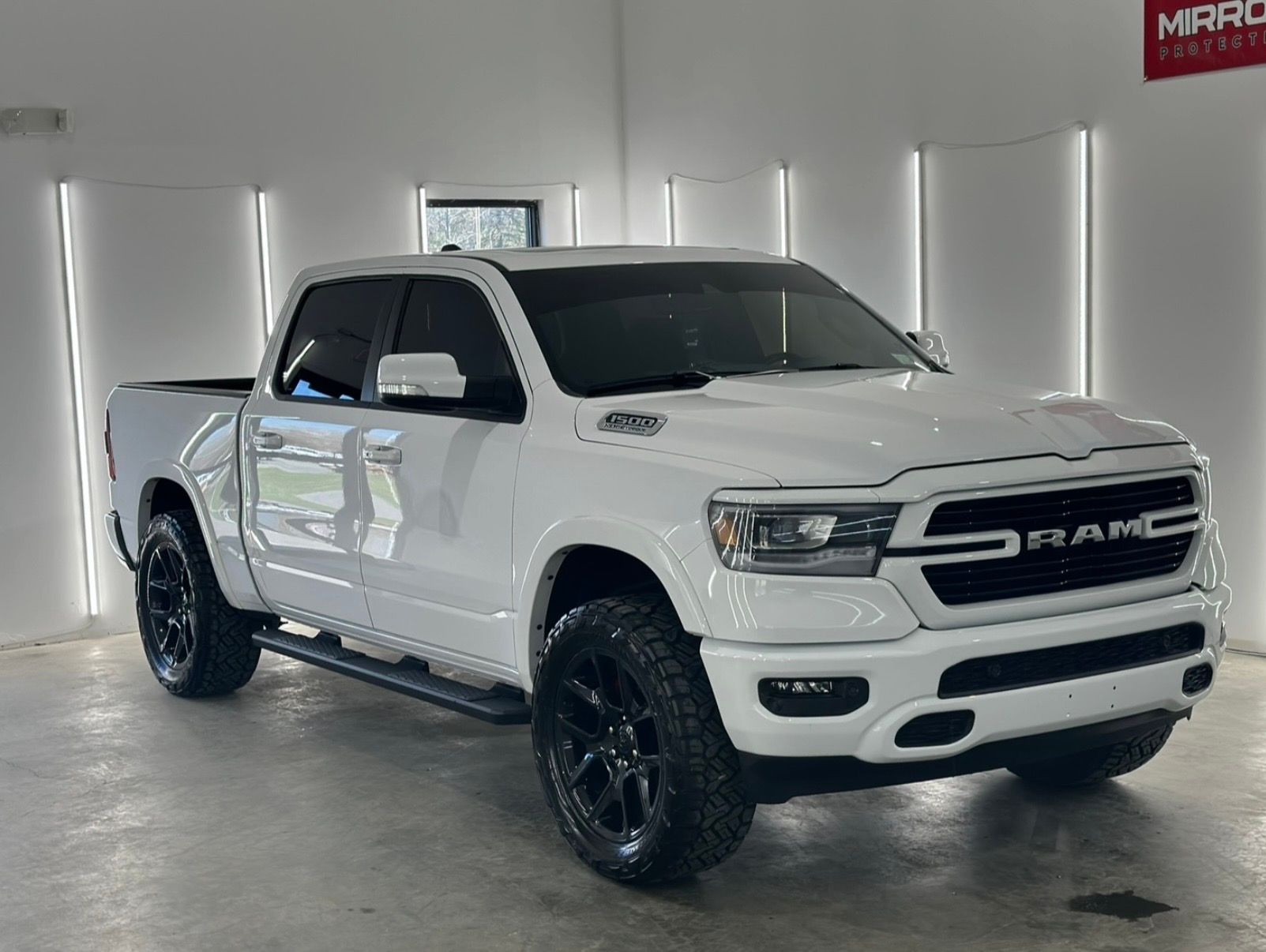 A white Ram pickup truck with black wheels parked in a brightly lit studio.