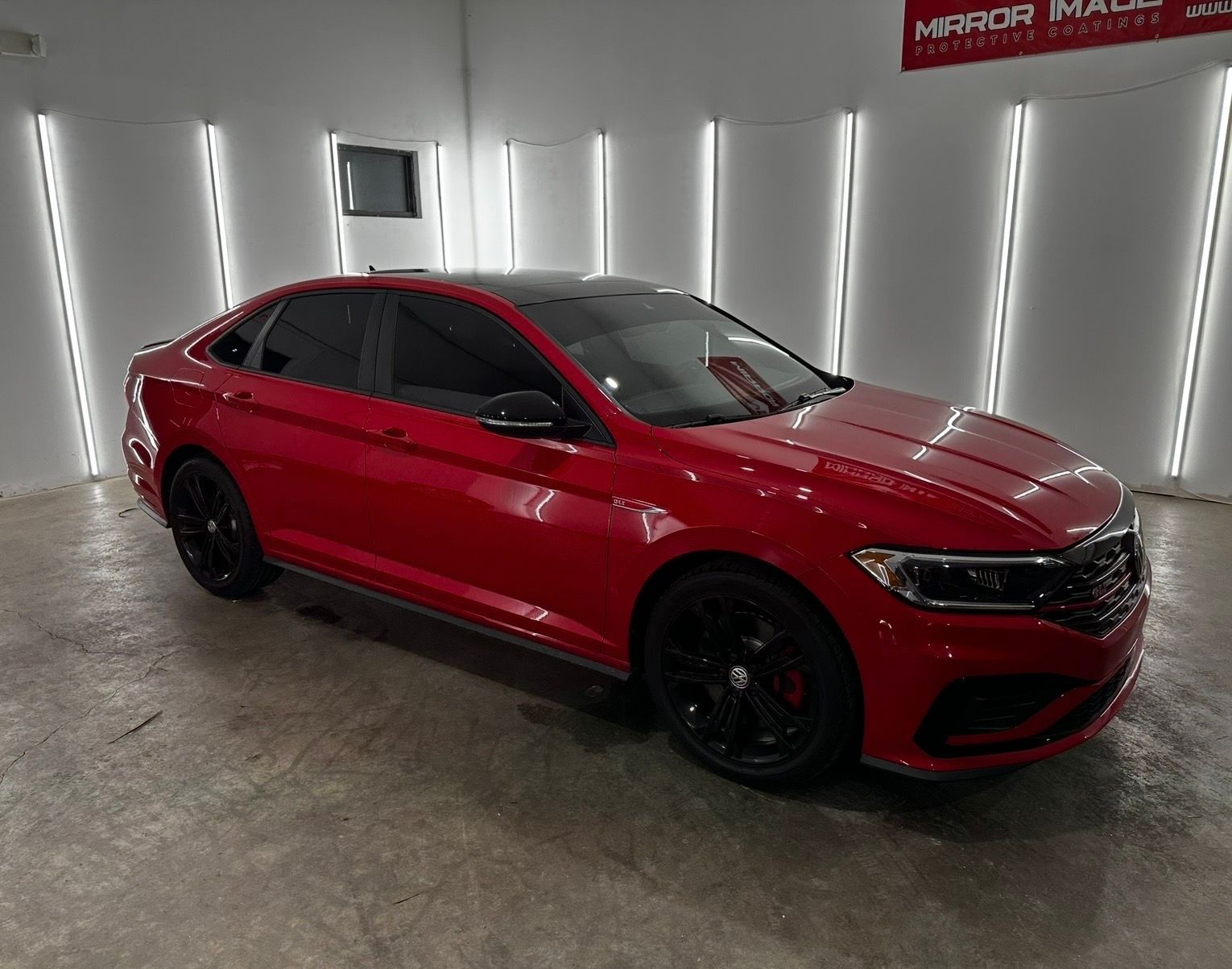 A bright red sedan with black rims and tinted windows parked in a bright, white-walled garage.