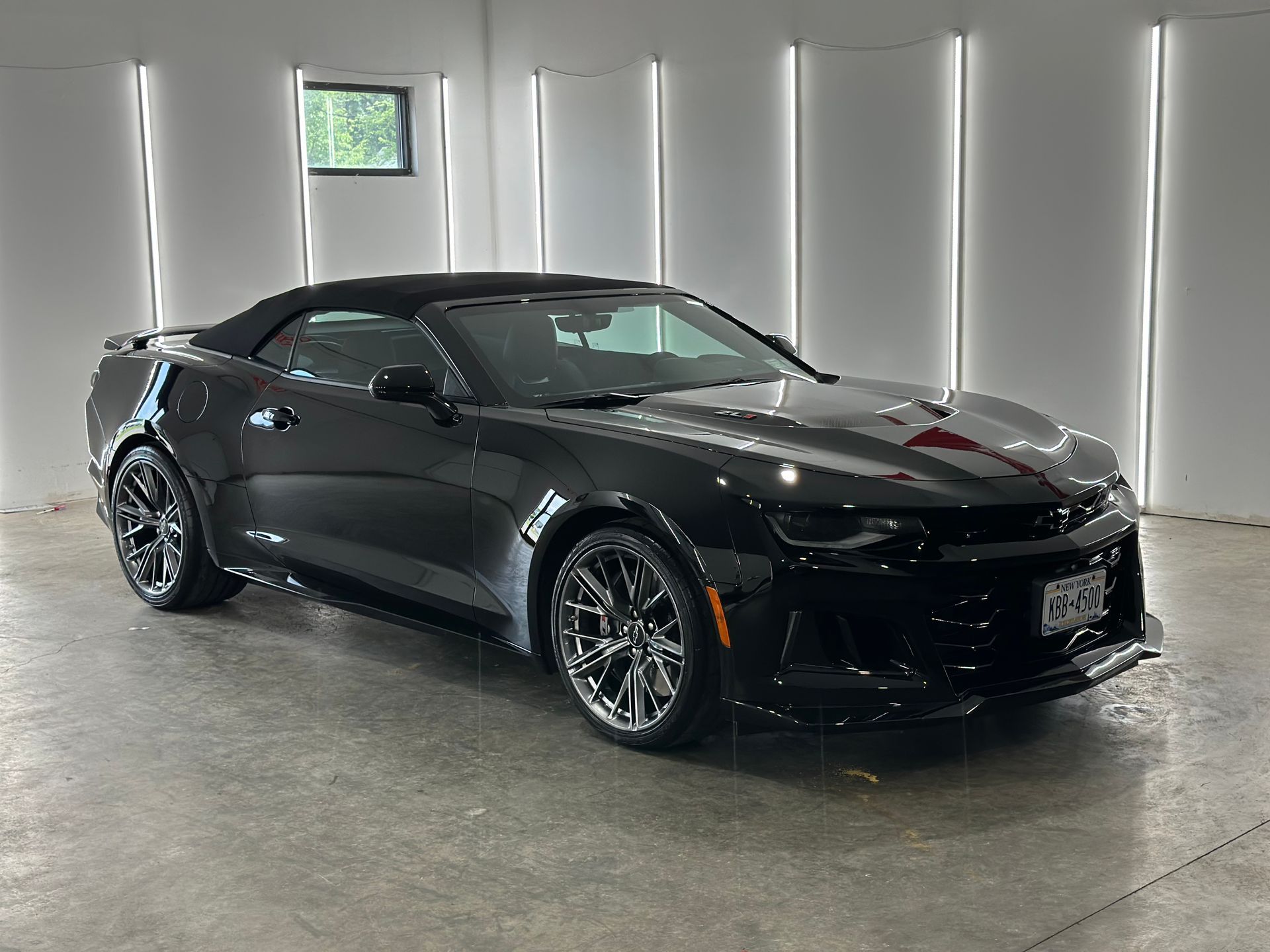 A black Chevrolet Camaro convertible parked in a bright, minimalist studio with white walls and vertical lighting.