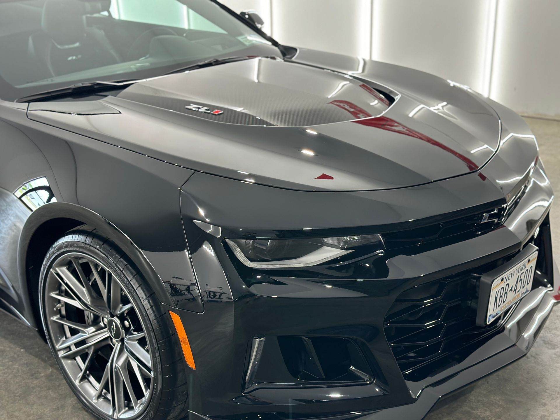 A black Chevrolet Camaro ZL1 parked in a well-lit indoor garage, showcasing its sporty design and carbon fiber hood.